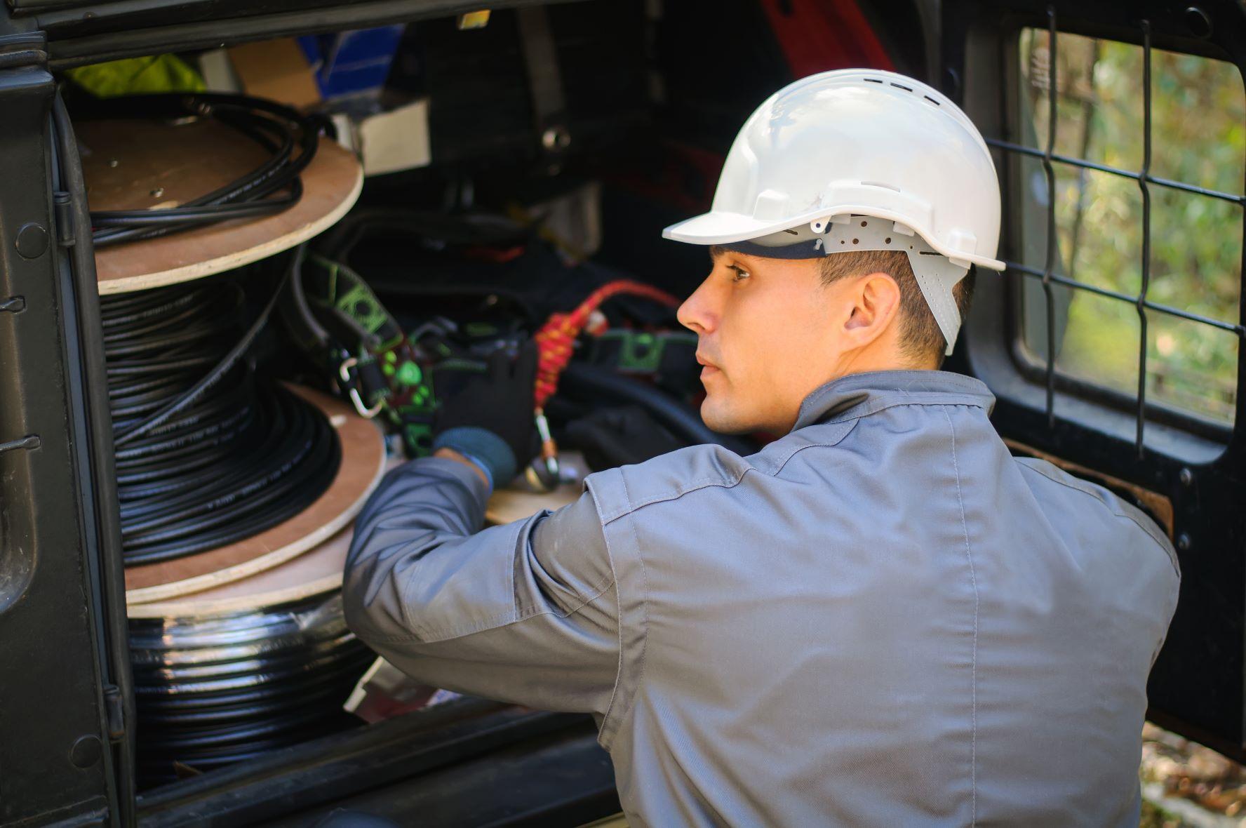 Technician wearing a white safety helmet working with fiber optic cable reels in the back of a service van.